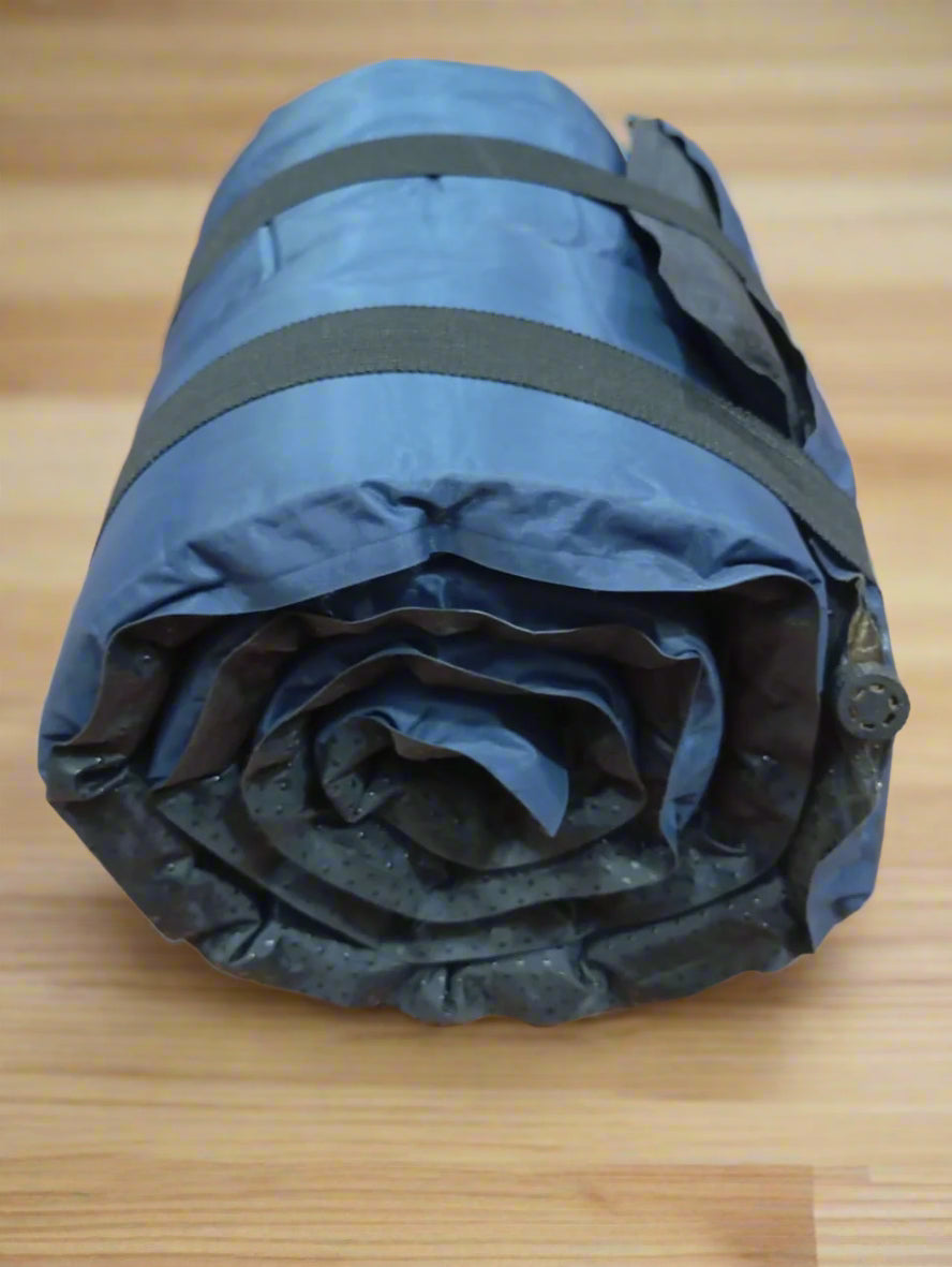 Rolled-up blue sleeping pad with black straps on a wooden floor