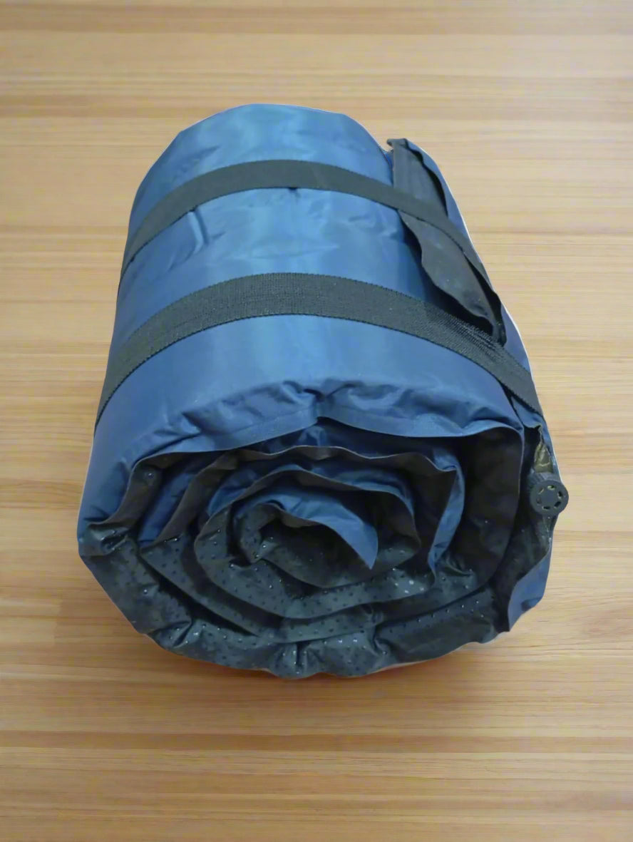 Rolled-up blue sleeping bag with black straps on a wooden floor